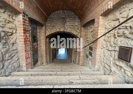 Republik San Marino, 7. September 2026. Eine Steintreppe führt durch einen Ziegel- und Steinbogen in einen engen Durchgang hinab. Ein Schild über dem A Stockfoto