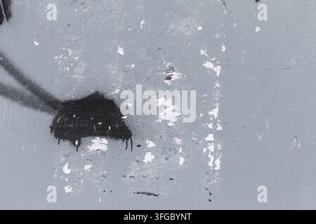 Vorderansicht einer schmutzigen und verwitterten urbanen Wand, die in Grau mit schwarzer Sprühfarbe und abgerissenen Plakaten gestrichen ist. Abstrakter Vollbild-Hintergrund mit distressierter Textur. Stockfoto