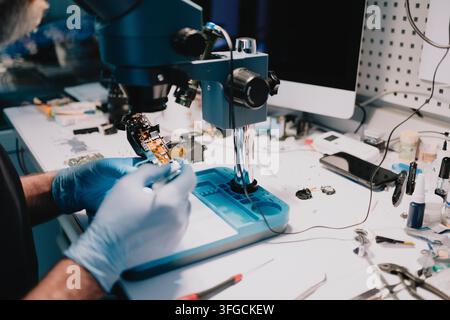 Techniker untersucht und repariert Miniatur-Elektronikbauteile unter einem Stereomikroskop an einem Service-Tisch und führt fortgeschrittene Diagnosen durch Stockfoto