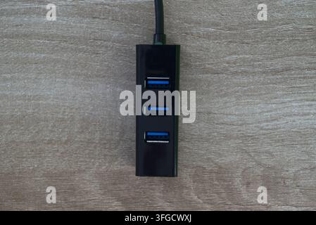 Symmetrische Ansicht von oben eines schwarzen Multiport-USB-Hubs mit blauen USB-Anschlüssen auf einem hellen Holz-Hintergrund. Stockfoto
