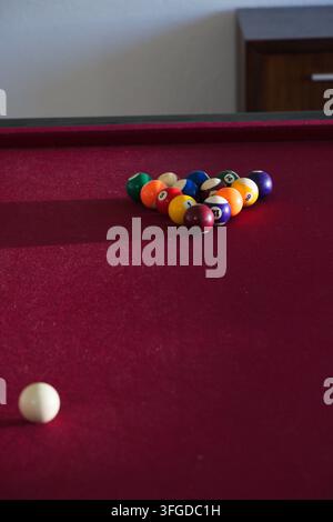 Dreieckiges Gestell mit bunten Billardkugeln, das auf einem kastanienbraunen Billardtisch nahe der Wand steht, mit ruhender Spielkugel Stockfoto