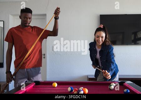 Verschiedenes Paar spielt Pool in einem Heimspielzimmer an einem rot bezogenen Tisch mit Queue und Bällen Stockfoto