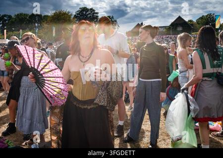 FRAU MIT ROSA FACH IN EINEM FESTIVAL, REPORTAGE, GREEN MAN FESTIVAL 2026, BRECON, WALES, UK, 2026: Unter einem dramatischen, bewölkten Himmel hält eine Frau mit roten Haaren und einem Korsettoberteil einen rosa Fächer, während sie in der Festivalmenge steht. Foto: Rob Watkins. INFO: Das Green Man Festival findet in den Brecon Beacons im August statt. Es feiert alternative Musik, Kunst, Literatur, Wissenschaft und familienfreundliche Kultur in einer wunderschönen Berglandschaft. Das Event 2026 fand während Regenschauern am Ende einer langen Hitzewelle und Dürre statt. Stockfoto