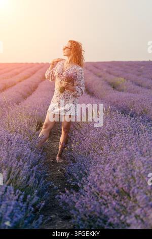Lavendelfeld, junge Frau mit lockigem Haar steht in einem blühenden violetten Lavendelfeld bei Sonnenuntergang und genießt die warme Sommersonne im Freien Stockfoto