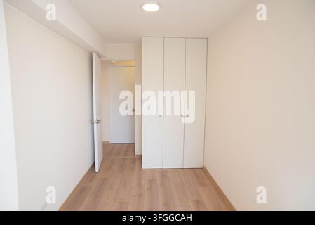 Leerer Raum mit Schrank: Ein sauberer, moderner leerer Raum verfügt über einen eingebauten weißen Schrank und hellen Holzfußboden, mit einer offenen Tür Stockfoto