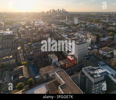 Eine Luftaufnahme über Aldgate und Whitechapel, Londoner Dächer bei Sonnenuntergang, mit Blick auf die Wolkenkratzer des Finanzdistrikts Canary Wharf am Horizont. Stockfoto