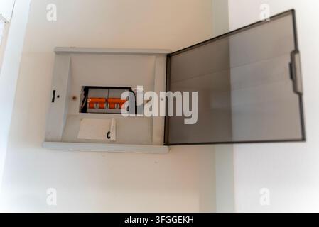 Offene wandmontierte elektrische Verteilerdose mit sichtbaren orangefarbenen Leistungsschaltern und Schutzabdeckung in einem Wohnraum. Stockfoto