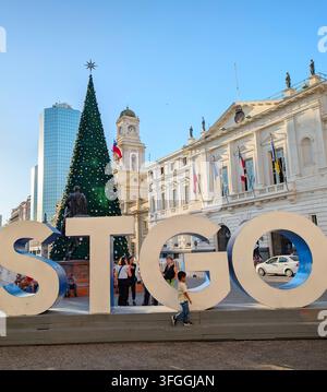 SANTIAGO, CHILE - 03. DEZEMBER 2025: Ein großes STGO-Schild steht in der Nähe eines hohen Weihnachtsbaums auf der Plaza de Armas mit historischen Gebäuden in der Nähe in Santiago, Chil Stockfoto