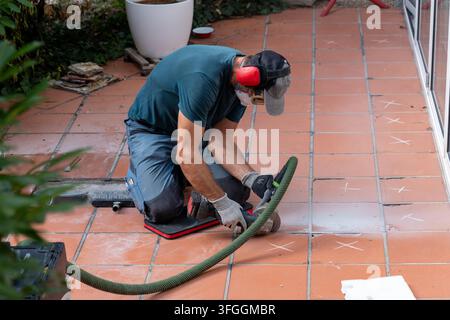 Ein Arbeiter schleift Terracottafliesen auf einer Außenterrasse mit Elektrowerkzeugen. Stockfoto