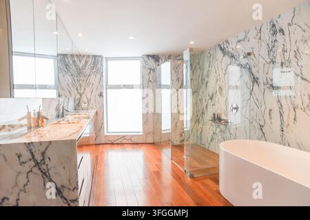 Modernes Luxusbad: Ein geräumiges und prächtiges Bad mit eleganten Marmorwänden, einer schlanken Badewanne und einer glasumschlossenen Dusche, alles beleuchtet Stockfoto