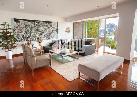 Modernes Wohnzimmer mit Weihnachtsbaum: Ein stilvolles und zeitgenössisches Wohnzimmer, das ein schlankes Ecksofa und schicke Sessel umfasst Stockfoto