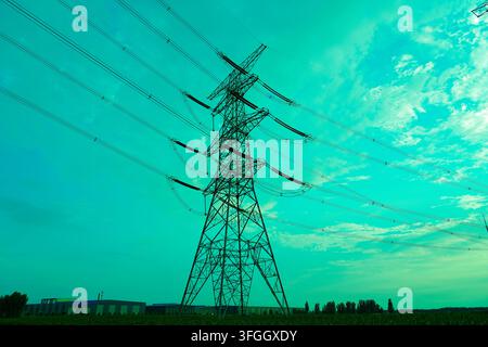 Hoher Stahl-Hochspannungsmast steht markant vor einem hellblauen Himmel, der mit weichen weißen Wolken übersät ist, und trägt dicke Stromübertragungsleitungen Stockfoto