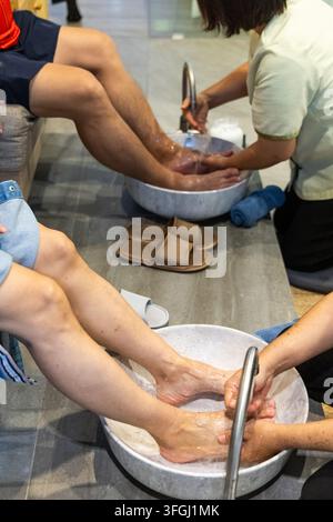 Nahaufnahme einer Masseurin, die die Füße und Beine des Kunden mit Wasser und Seife wäscht, bevor sie eine traditionelle thailändische Fuß- und Beinmassage im Salon durchführt. Stockfoto