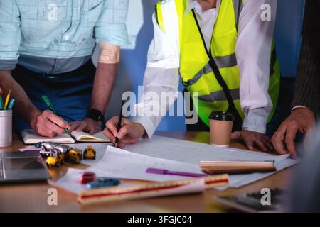Baumanagement-Team bespricht Gebäude-layoutpapier auf dem Schreibtisch. Nahaufnahme einer Hand beim Schreiben. Konzept der Projektplanung, Zeitplan der Arbeiten, Stockfoto