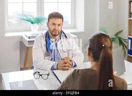 Ernster männlicher Arzt in der Klinik trägt weiße Arztkleidung, spricht, diskutiert über Gesundheitsergebnisse Stockfoto