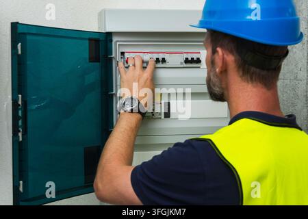 Nahaufnahme eines Elektrikers mit blauem Schutzhelm, der eine Sicherungskastenabdeckung überprüft Stockfoto