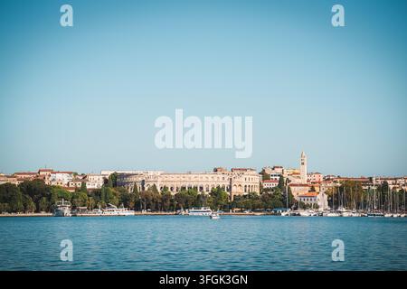 Blick auf das antike römische Amphitheater, Boote, die im Hafen angelegt sind, und historische Gebäude unter einem klaren blauen Himmel in Pula, Istrien, Kroatien. Stockfoto