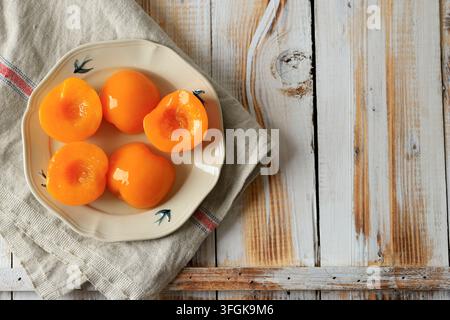 Goldene Dosenpfirsichhälften in leichtem Sirup, angeordnet auf weißer Keramik und weichem Leinenstoff Stockfoto