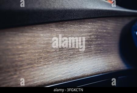 Nahaufnahme des Interieurs eines modernen Luxusautos mit einer Türverkleidung aus texturiertem Naturholz mit offenporiger Holzmaserung und dunklem Leder. Stockfoto