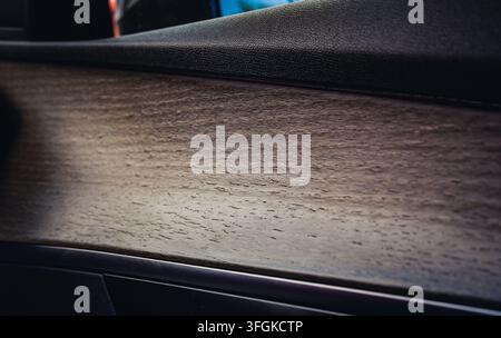 Nahaufnahme des Interieurs eines modernen Luxusautos mit einer Türverkleidung aus texturiertem Naturholz mit offenporiger Holzmaserung und dunklem Leder. Stockfoto