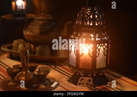 Arabische Lampe, die Licht mit Teekrug und Tasse auf dem Tisch in der Dunkelheit spendet Stockfoto