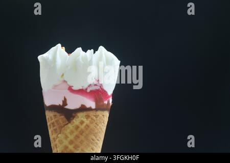 Erdbeergeschmack-Topping aus geschlagener Sahne in einer Waffeltüte, Eiscreme arrangiert auf schwarzem Hintergrund Stockfoto