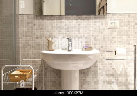 Weißes keramisches Wandspülbecken mit Chrom-Wasserhahn steht in der Nähe einer Mosaikfliesenwand. Stockfoto