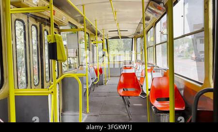 Die leere Straßenbahn fährt am sonnigen Sommertag entlang der Stadtstraße. Die ruhige Straße und die vorbeifahrende Straßenbahn halten das urbane Leben und moderne öffentliche Verkehrsmittel in Bewegung Stockfoto