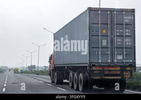Container-LKW fährt auf einer breiten Autobahn unter einem bewölkten Himmel, mit freiem Straßenraum links für Text, geeignet für Transport, Logistik, Stockfoto