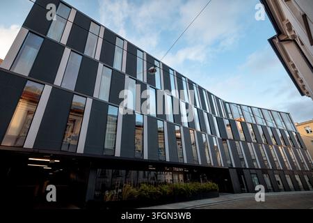 Gekrümmtes zeitgenössisches Bürogebäude mit abwechselnd dunkler Verkleidung und vertikalen Fenstern spannt sich über eine schmale Straße im Stadtzentrum. Stockfoto