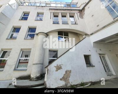 Niedrigwinklige Ansicht einer verwitterten weißen Wohn- oder Institutsgebäudefassade mit eklektischen architektonischen Elementen. Die Struktur zeigt Stockfoto