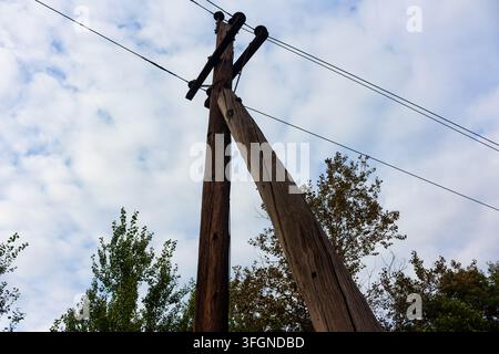Alter hölzerner Strommast mit einer Stützstrebe, der hoch gegen einen bewölkten Himmel ragt, mit verwitterter Holztextur und sich erstreckenden Stromleitungen, die vorbeiführen Stockfoto