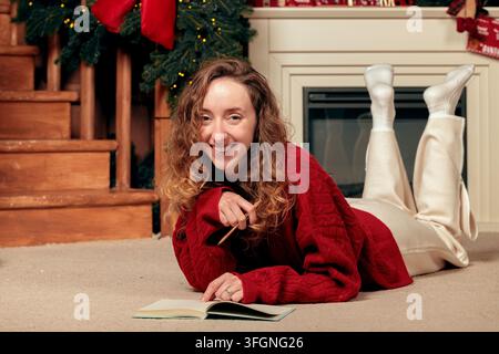 fröhliches lächelndes Porträt einer jungen erwachsenen Frau, die auf einem mit Weihnachtsdekoration geschmückten Boden liegt Stockfoto