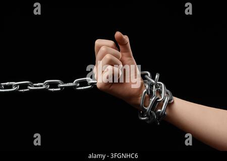 Unterdrückungs- und Gefangenschaftskonzept menschliche Hand, die mit einer schweren Metallkette gefesselt ist, kämpft gegen Einschränkung und Mangel an Freiheit auf schwarzem Hintergrund Stockfoto