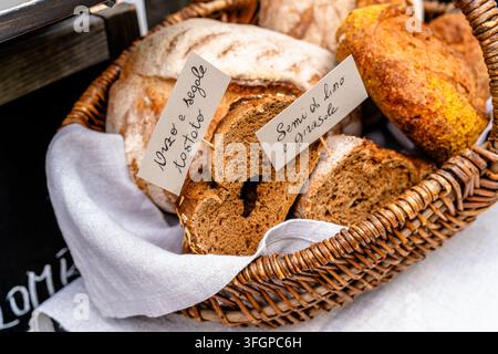 Verschiedene geschnittene und ganze handwerklich hergestellte Brote, die in einem Weidenkorb mit handgeschriebenen Etiketten präsentiert werden, geeignet für Themen wie Bäckerei, Lebensmittelmarkt und Einzelhandel. Stockfoto