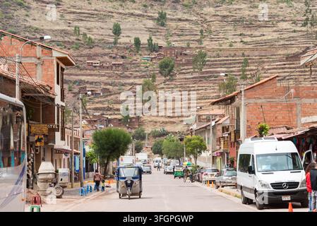 Eine lebendige Straßenszene in Pisac, Peru, zeigt die traditionelle Architektur der Stadt, die sich vor dem Hintergrund alter landwirtschaftlicher Terrassen befindet. Loca Stockfoto