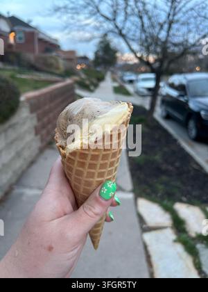 Frau hält ein Eis am Stiel, während sie in einer Nachbarschaft in der Dämmerung spazieren geht Stockfoto