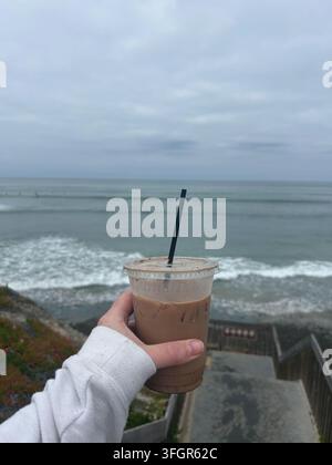 Hält einen Eiskaffee mit Blick auf den Ozean Stockfoto