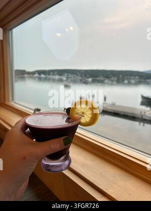Frau hält lila Cocktail mit Hafenblick in Southwest Harbor, Maine Stockfoto