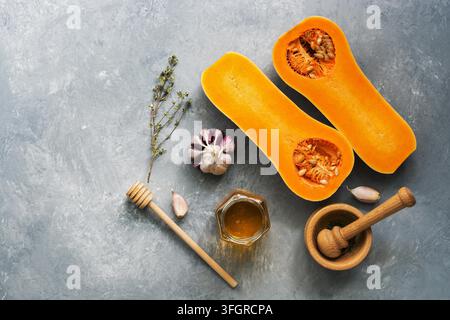 Hälften der rohen Kürbis oder Butternut-kürbis mit Kräutern, Honig und Knoblauch für das Kochen auf Grau im Hintergrund. Ansicht von oben, flach Stockfoto