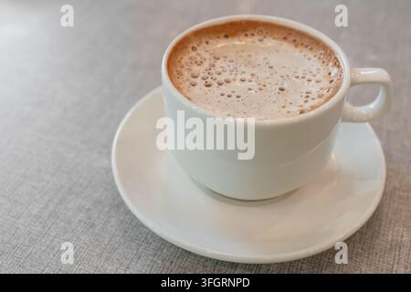 Eine frisch gebrühte Tasse cremiger Kaffee, gekrönt mit feinem Schaum, serviert in einer weißen Keramiktasse mit Untertasse Stockfoto