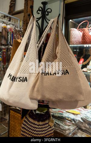 Traditionelle malaysische gewebte Markttaschen, die in einem Souvenirladen präsentiert werden, mit cremefarbenen Netzdesigns und der Aufschrift „MALAYSIA" Stockfoto