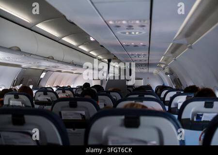 Innenansicht einer Flugzeugkabine mit Reihen von Passagiersitzen und Gepäckfächern über den Sitzen, Passagiere im Hintergrund Stockfoto