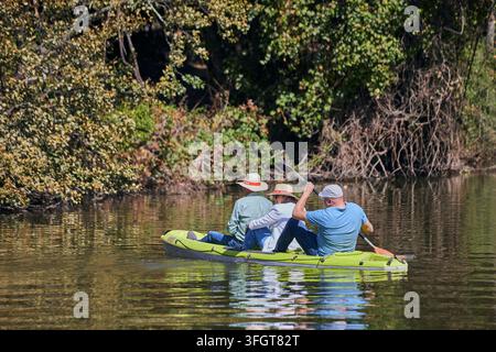 Drei Besucher paddeln ein grünes Kajak durch eine bewaldete Flusslandschaft, von hinten betrachtet, während sie sich auf das schattige Flussufer in Andalusien, Spanien, zubewegen. Stockfoto