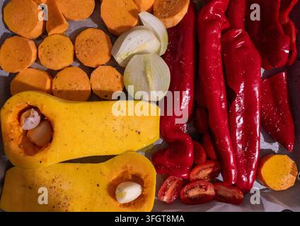 Oberblick über farbenfrohe frische Gemüse, die zum Backen im Ofen auf einem Backblech vorbereitet sind, einschließlich Butternusskürbis-Hälften mit Knoblauch, Süßkartoffelscheiben Stockfoto