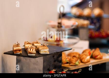 Köstliche Vorspeisen auf schwarzer Schieferplatte. Frische Backwaren und farbenfrohe Früchte im Hintergrund. Elegante Buffet-Anordnung für gehobene Veranstaltungen oder Restaurants. Ich Stockfoto