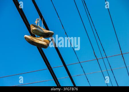 Paar abgetragener senfgelber Skateschuhe, die über Stromleitungen in East Vancouver, British Columbia, zusammengebunden hängen. Stockfoto
