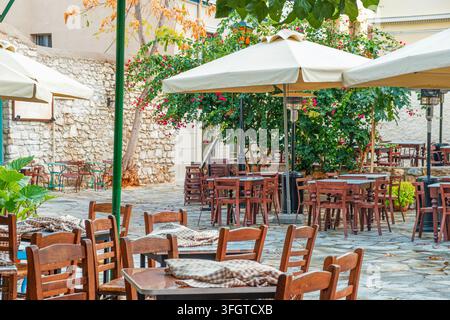 Außenrestaurant-Terrasse mit Holztischen, Stühlen und großen Sonnenschirmen auf einer mit Stein gepflasterten Straße in Athen, Griechenland. Mediterranes Essen, Sommer Stockfoto