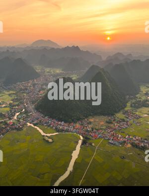 Luftbild des Bac-Son-Tals mit üppigen grünen Reisfeldern, einem sich windenden Fluss und Dorfhäusern, die sich zwischen Karstbergen während eines goldenen Sonnenuntergangs befinden Stockfoto