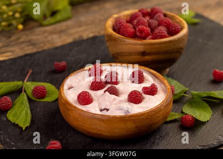 Pink-Berry-Joghurt mit roten Himbeeren, Naturjoghurt gemischt mit reifen Himbeeren auf einer dunklen Steinfliese Stockfoto